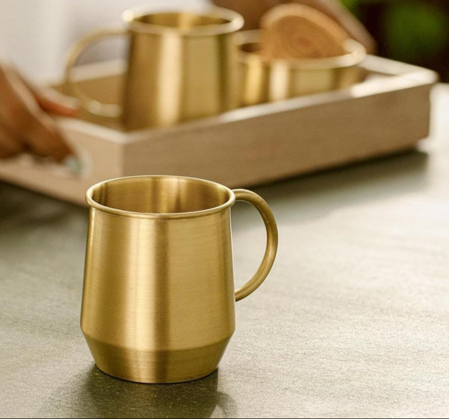 Gold mug on a table with a blurred background of a person holding a tray with more mugs.